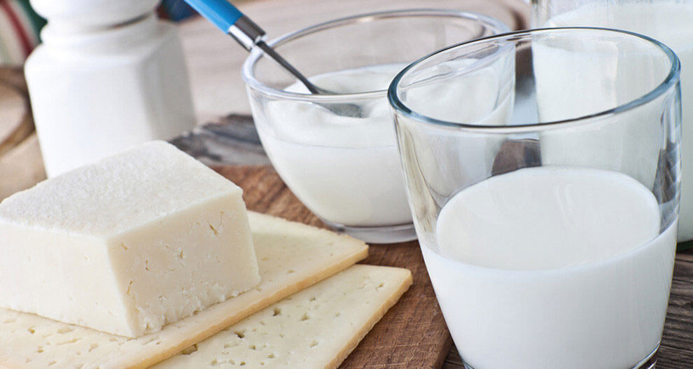 A glass of milk, a bowl of yogurt, cheese, and crackers on a wooden table.